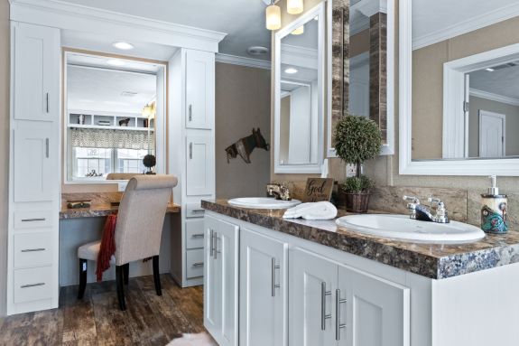 The Drake primary bathroom has a separate tub and shower, double sinks and a built-in vanity with cabinets surrounding it, overhead lighting and a large mirror.