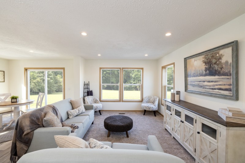 Living room of a Tempo manufactured home with neutral couches, chairs and an entertainment enter, with white walls and light wood trim