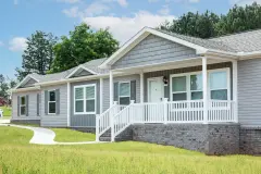 The exterior of a manufactured home with gray siding, roof and skirting and white trim in a neighborhood.