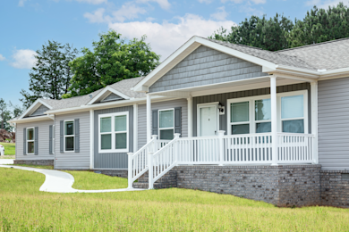 The exterior of a manufactured home with gray siding, roof and skirting and white trim in a neighborhood.