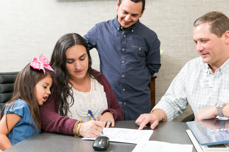 Woman signing paperwork at a home center with husband, daughter and home center consultant. 