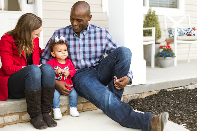 Man and woman with small child sitting on the porch of their manufactured home.