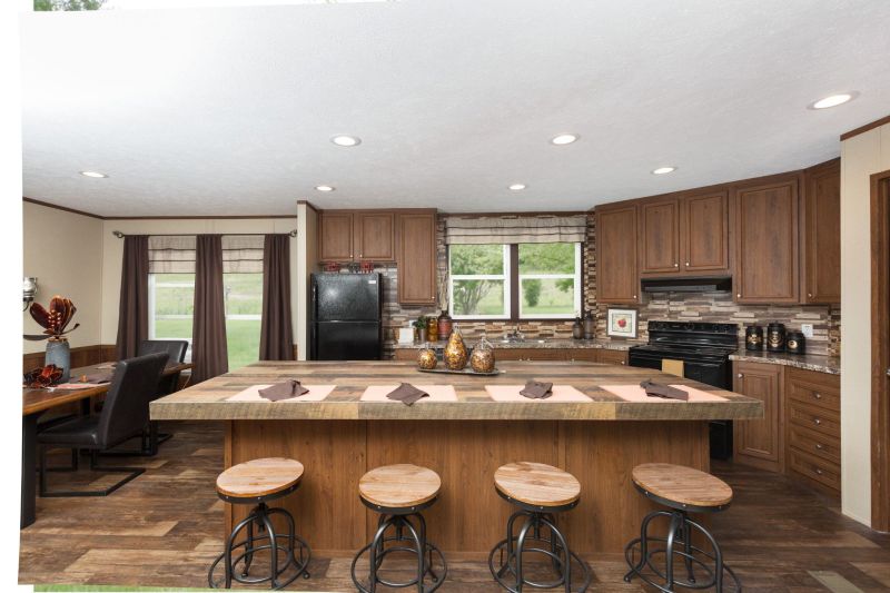 Kitchen with large island with short stools pulled up to it. The dining area is off to the side and brown cabinetry lines the kitchen area.