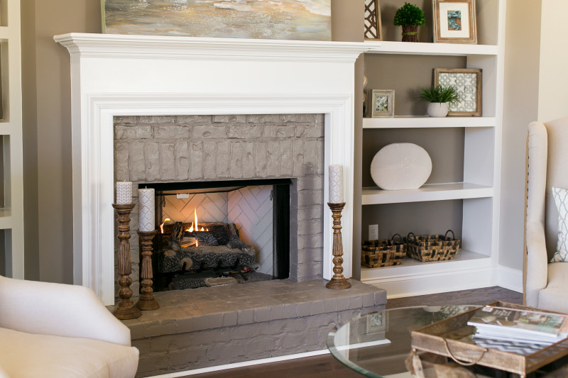  A white fireplace with an inner brick chamber that's been painted gray. There's a white built in book shelf to the right of it with decor displayed on it.