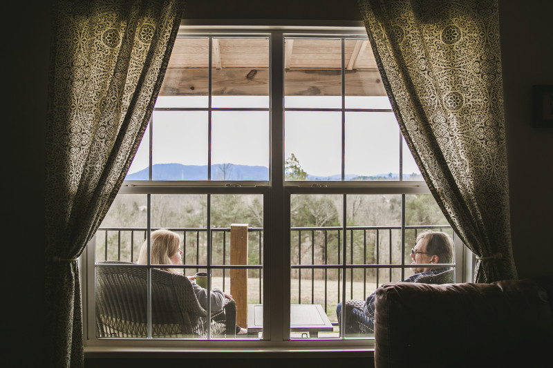 Husband and wife sit on their front porch looking out at the mountains