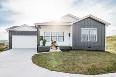 A couple sits with their dog on the front porch of a modular home with gray and white siding and an attached garage.