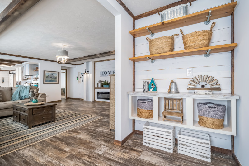 Entryway of a manufactured home with a shiplap accent wall, 2 shelves with baskets and a built-in shelf with cubbies, leading into the living room.