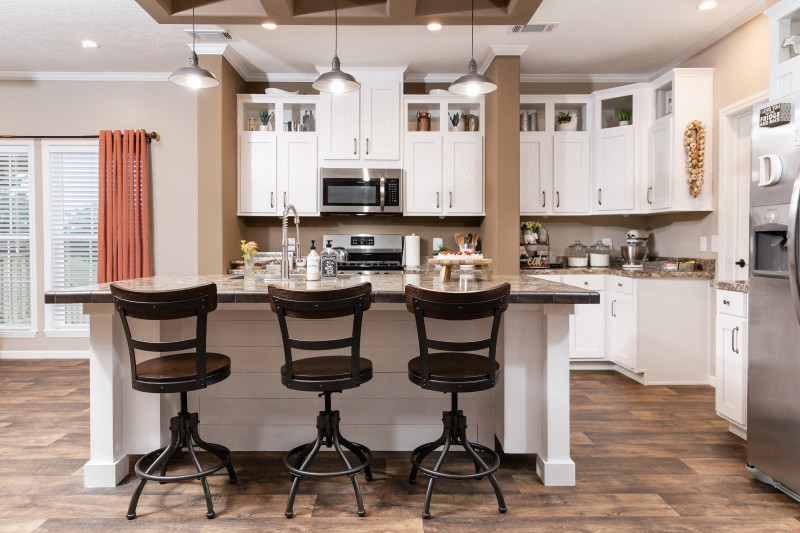 Custom prefab home kitchen with shiplap island, round stools, white cabinets, pendant lighting and coffered ceiling