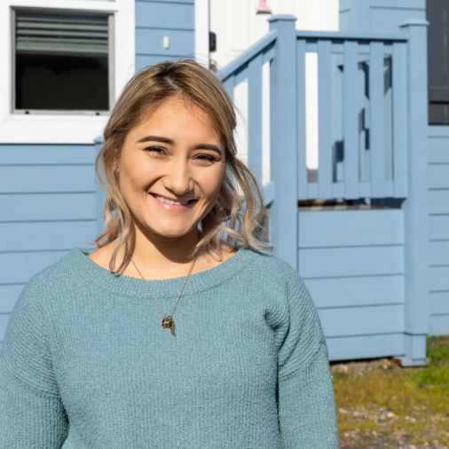 Maria Cibrian stands outside of her blue and white Clayton manufactured home in California.