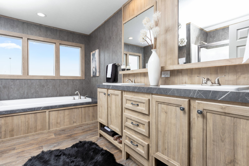 Side view of the primary bathroom shows double vanity with mirrors hanging over it. There is a soak tub off to the side with three windows over it.