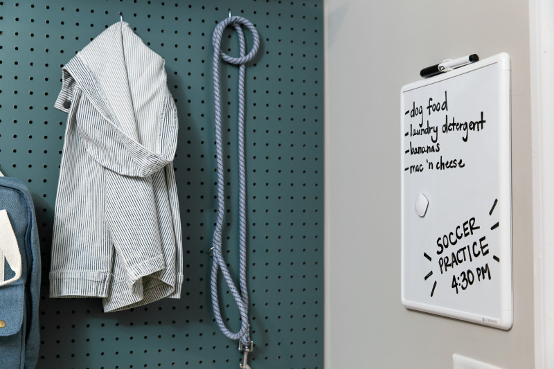 Green pegboard with jacket and dog leash hanging on the wall next to a white board