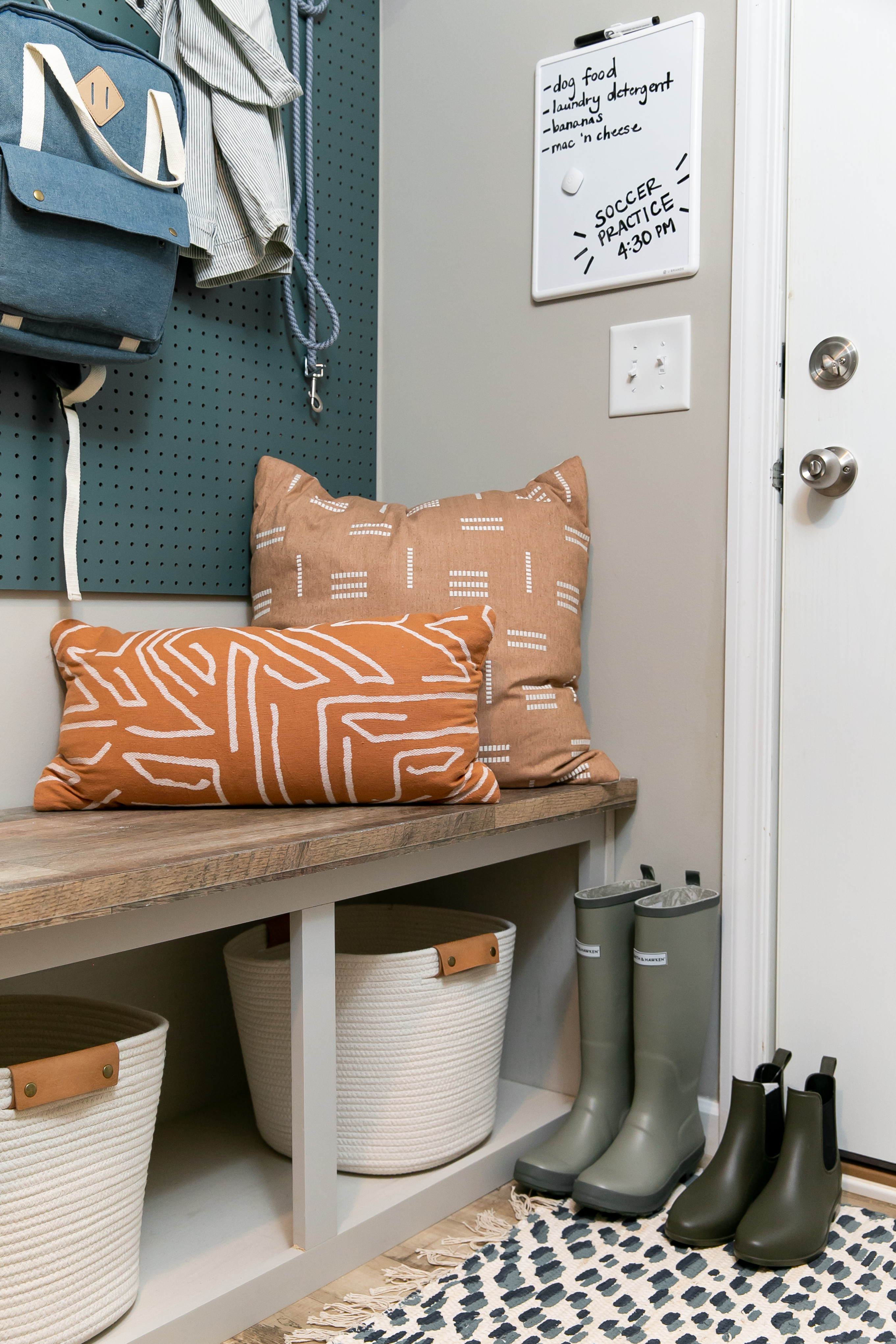 Entryway of a Clayton manufactured home with a bench with pillows, cubbies underneath, a pegboard on the wall and boots next to the door