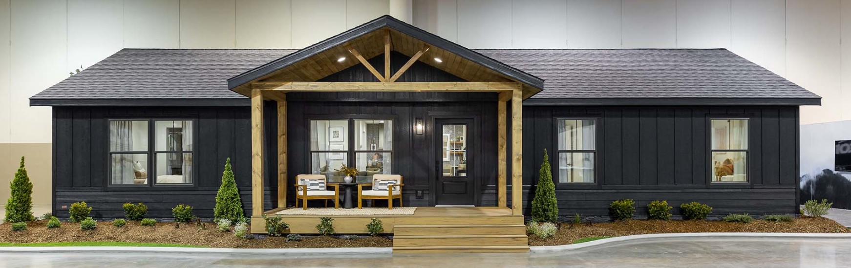 Exterior image of a dark colored manufactured home with a natural wood front porch. The home is net-zero electricity. 