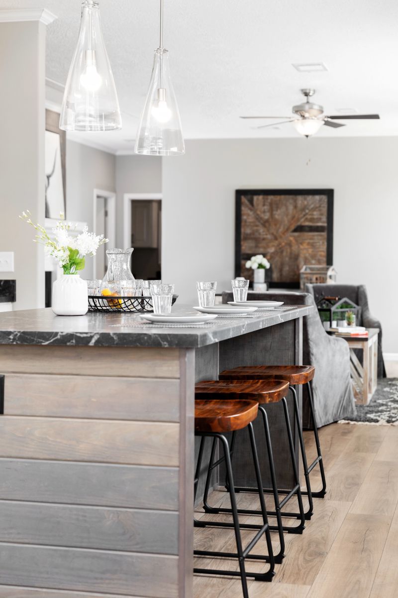 Kitchen with partial view of island with wooden base and black countertop. There are two clear hanging light fixtures suspended over it.