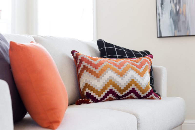 Orange, plum and black decorative pillows on a white couch.