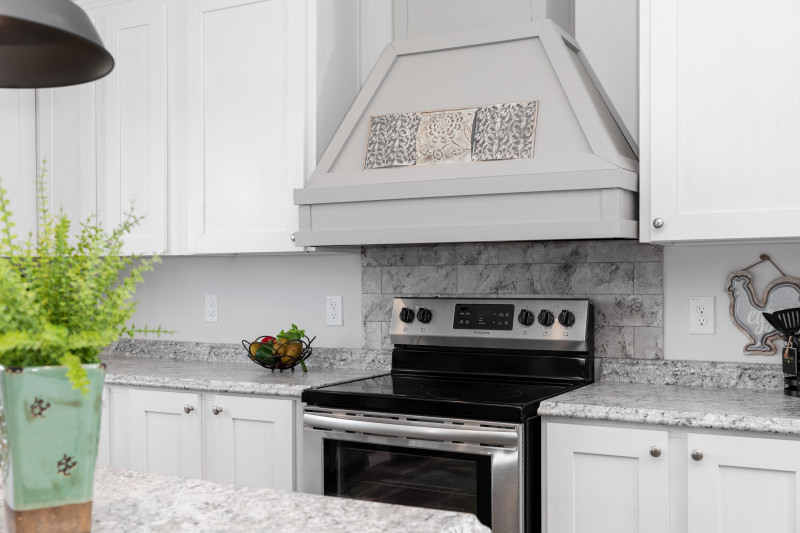 The kitchen of the Palmetto model with black appliances, white cabinets and a large gray range hood.