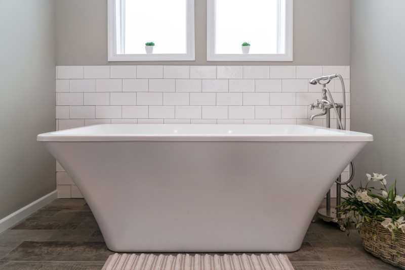 Soaking tub centered in shot with tile backsplash and windows.
