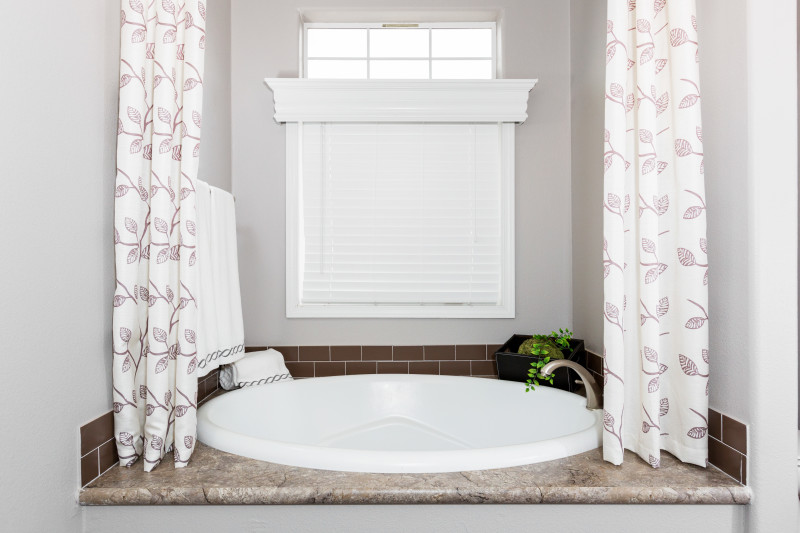 A round sunken garden tub in a manufactured home bathroom with a window and storage space around it.