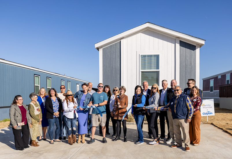 People cut a blue ribbon and cheer in front of a home 