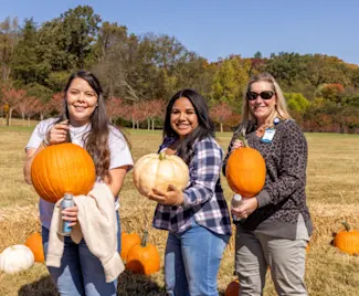 Three Clayton team members each hold up a pumpkin at the company fall festival.