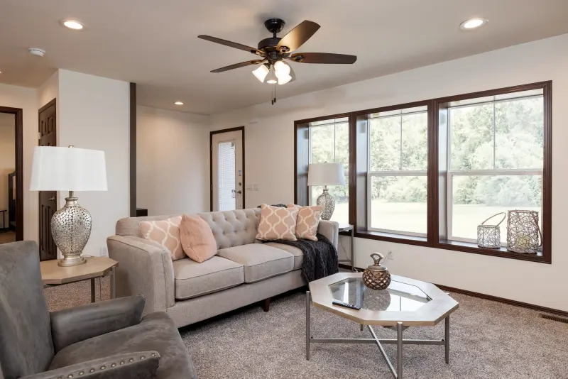 There's a bright, white living room  with neutral colored decor and three windows framed in dark wood. 