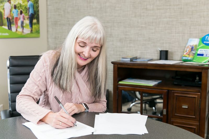 Woman smiles while she signs paperwork while sitting at a table in a home center.