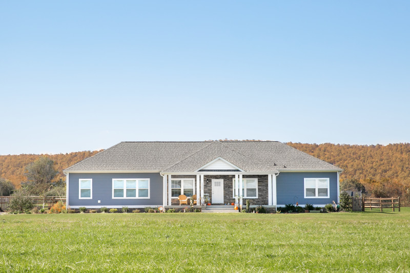 Manufactured home with blue siding and a stone front porch with a large front yard.