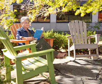 A Clayton team member sits outside on one of three colorful Adirondack chairs while reading a book.