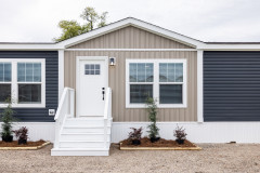 Exterior of Clayton Tempo home with tan and dark blue siding, white trim, small white porch and a white front door.