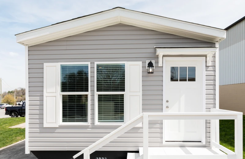 The exterior of a front-loaded manufactured home with gray siding and a white door, porch and shudders.