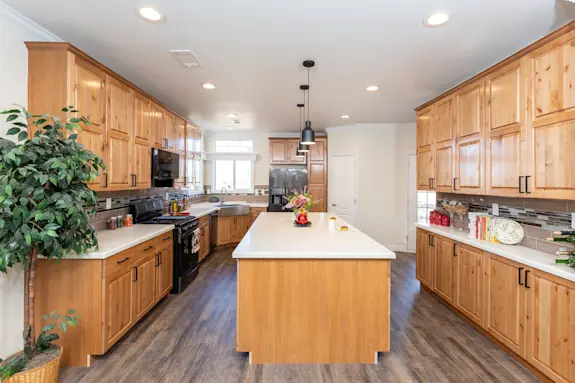 The [model name] has a lot to offer with this a kitchen full of counterspace, wood cabinets, a pantry and a partitioned dining room on the other side, as well as a wrap-around porch and luxurious primary bedroom suite.