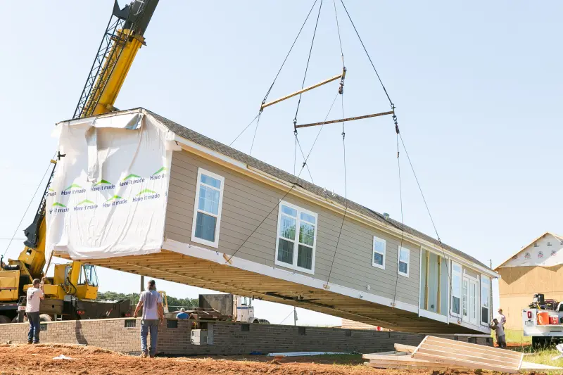 A modular home is being hoisted by a crane over a foundation.