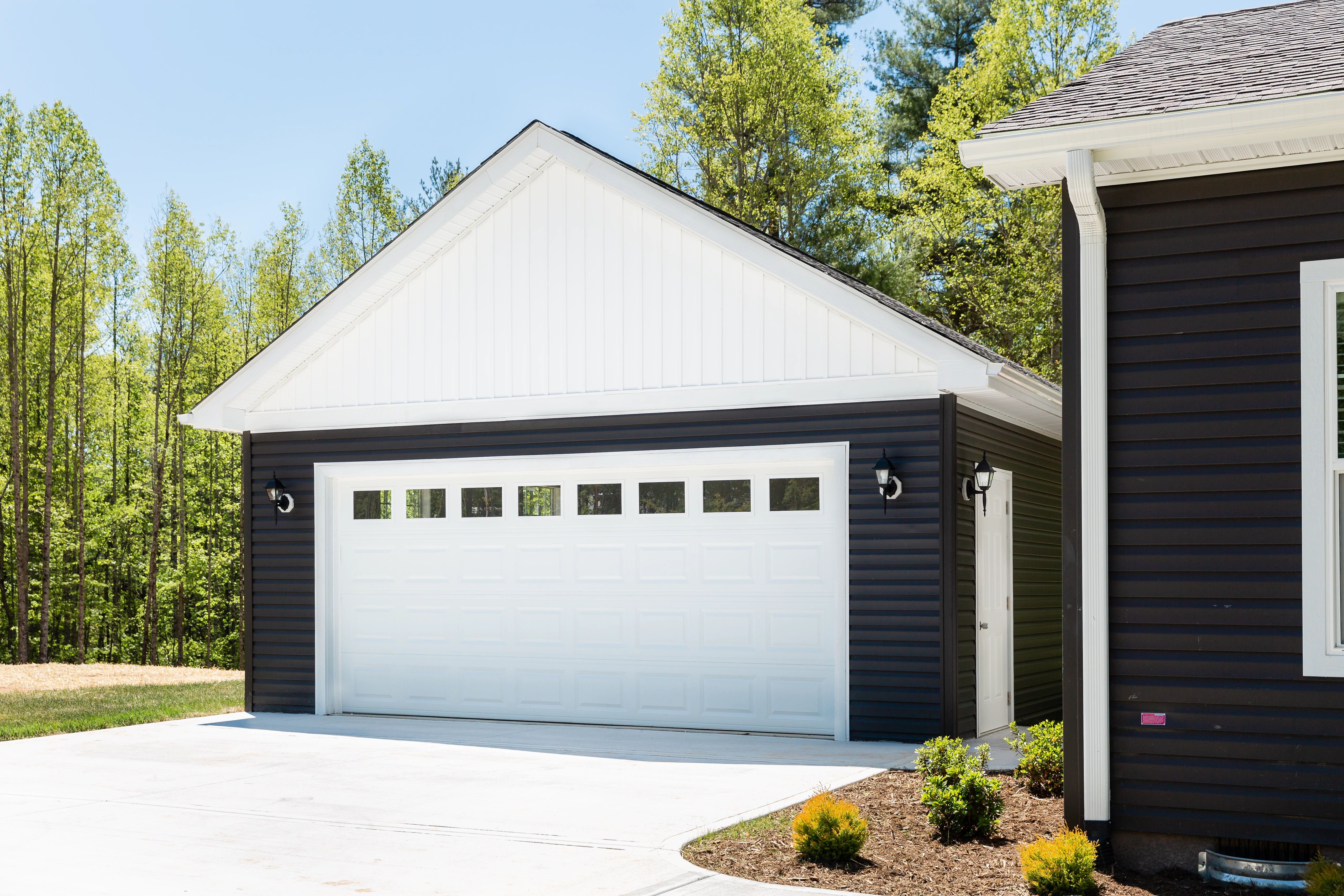 A detached garage next to a manufactured home with dark siding and white door and trim.