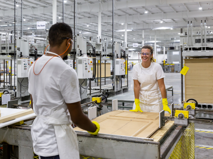 Two team members wearing white and gloves work on making a door.