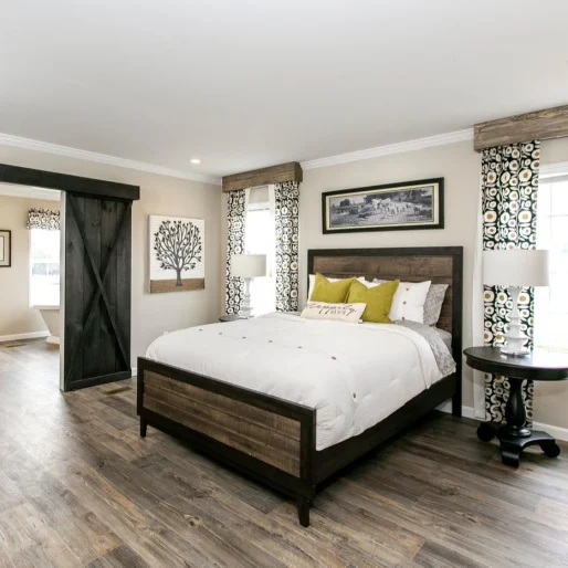 [model name] bedroom features wood style flooring and sliding barn doors that open up to a private bathroom space.
