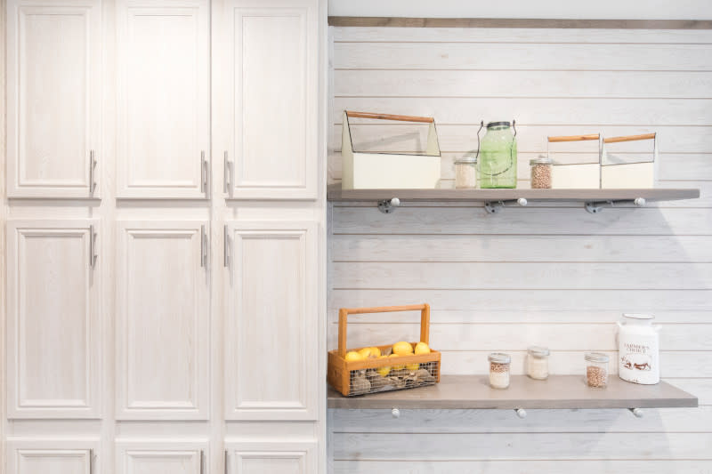 2 light wood shelves with assorted jars and baskets on a cream shiplap wall with cream cabinets to the left of it.