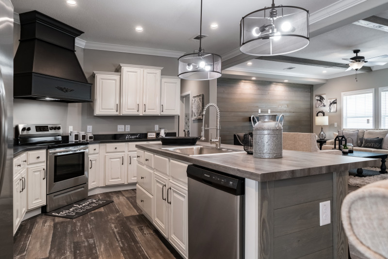 Manufactured home with open floor plan, kitchen island and black rustic hood vent.