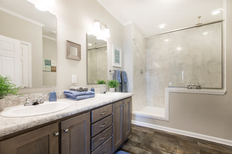 A manufactured home primary bathroom with a double-sink vanity and a large walk-in tile shower with a half-glass enclosure.