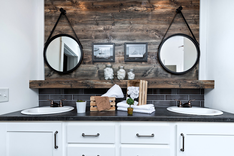 Manufactured home bathroom with double sinks and wooden accent wall.