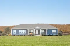 Blue modular home outside with a large yard.