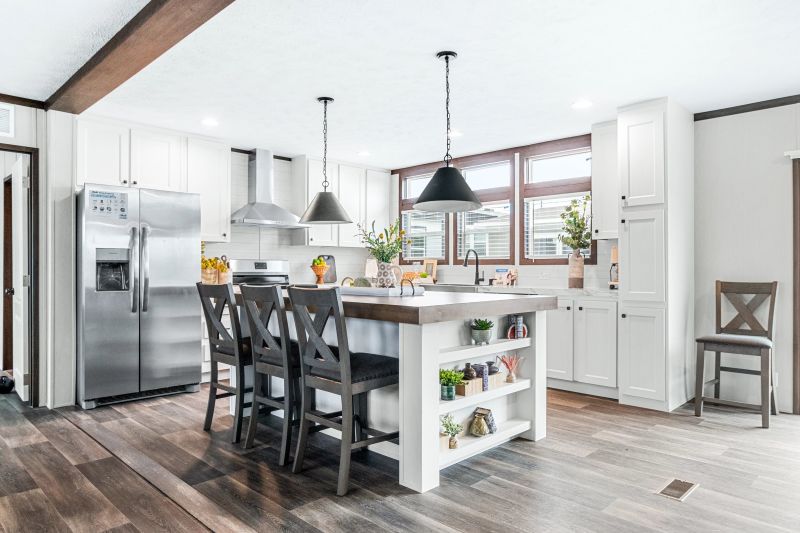 There's a white kitchen with three windows above the sink and brown chairs pulled up to a kitchen island.