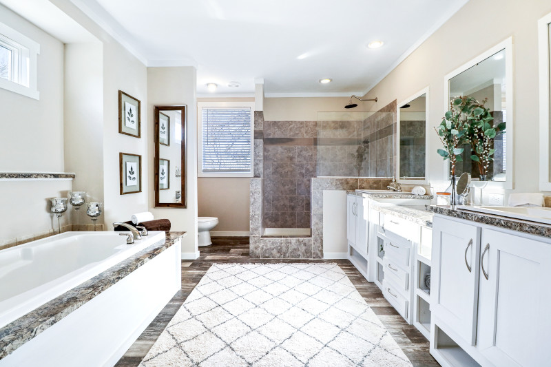 A primary bathroom with white cabinets and dual vanity, a soaker tub, a walk-in shower and a fluffy white rug.