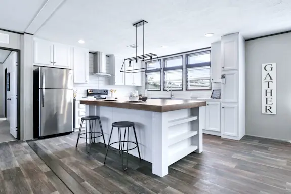 The [model name[ features stainless steel appliances and a large island with built-in shelves.