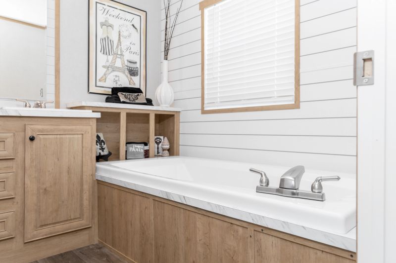 Primary bathroom of a Clayton manufactured home with shiplap accent wall, light wood vanity and cubbies and a bathtub.