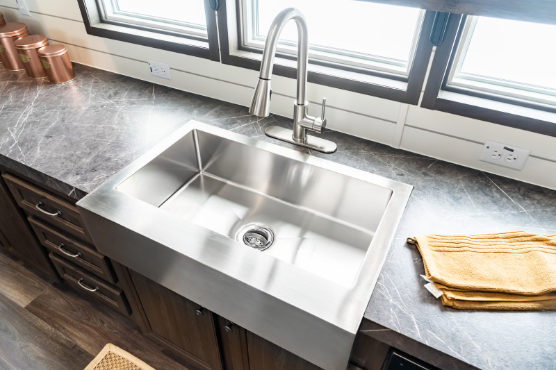 Top-down view of a stainless-steel sink. There are windows with light shining through and a gray, marble-styled countertop.