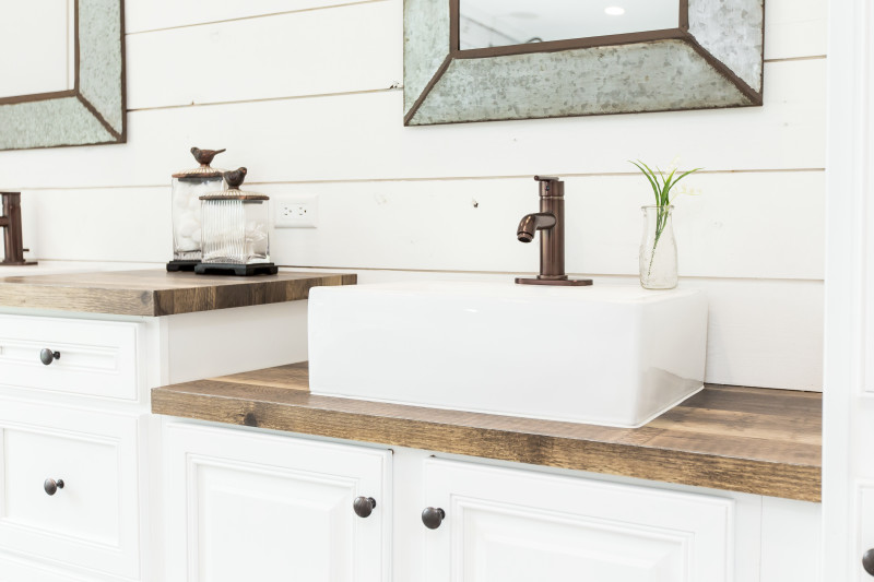 Manufactured home bathroom with medium wood style, stair step countertop, white porcelain raised sink, white cabinets, shiplap accent wall behind and galvanized metal mirrors.