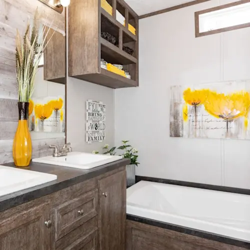 The bathroom in The Anniversary 76 features dual sinks and a garden tub with built-in shelves above it.