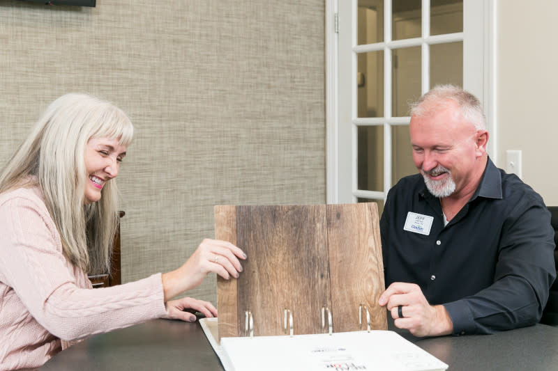 Woman looks at a book of flooring options with a home consultant at a table in a home center