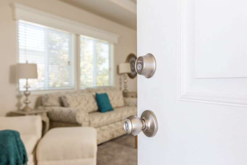 Silver Kwikset door handle in a white door, leading into a living room.