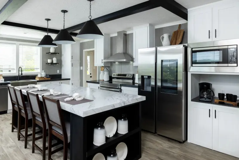 Manufactured home kitchen with white cabinetry and black accents. There's a black island with white marbled top in the center of the kitchen.